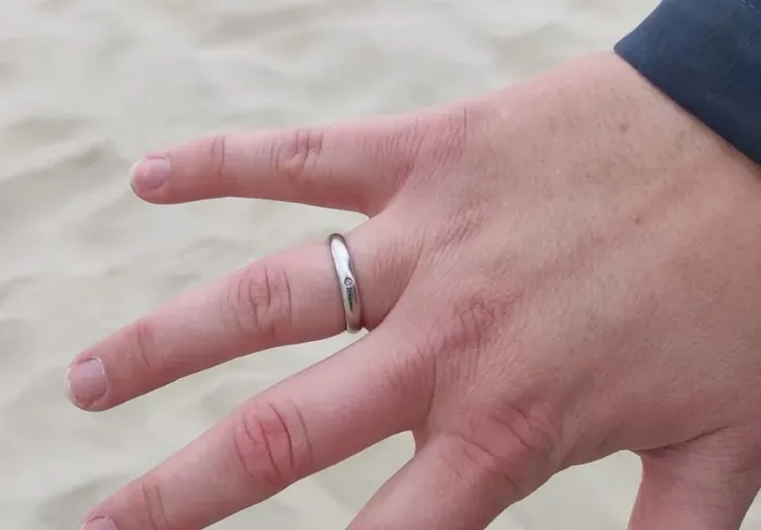 Goldring im hellen Strandsand, daneben ein Pinpointer